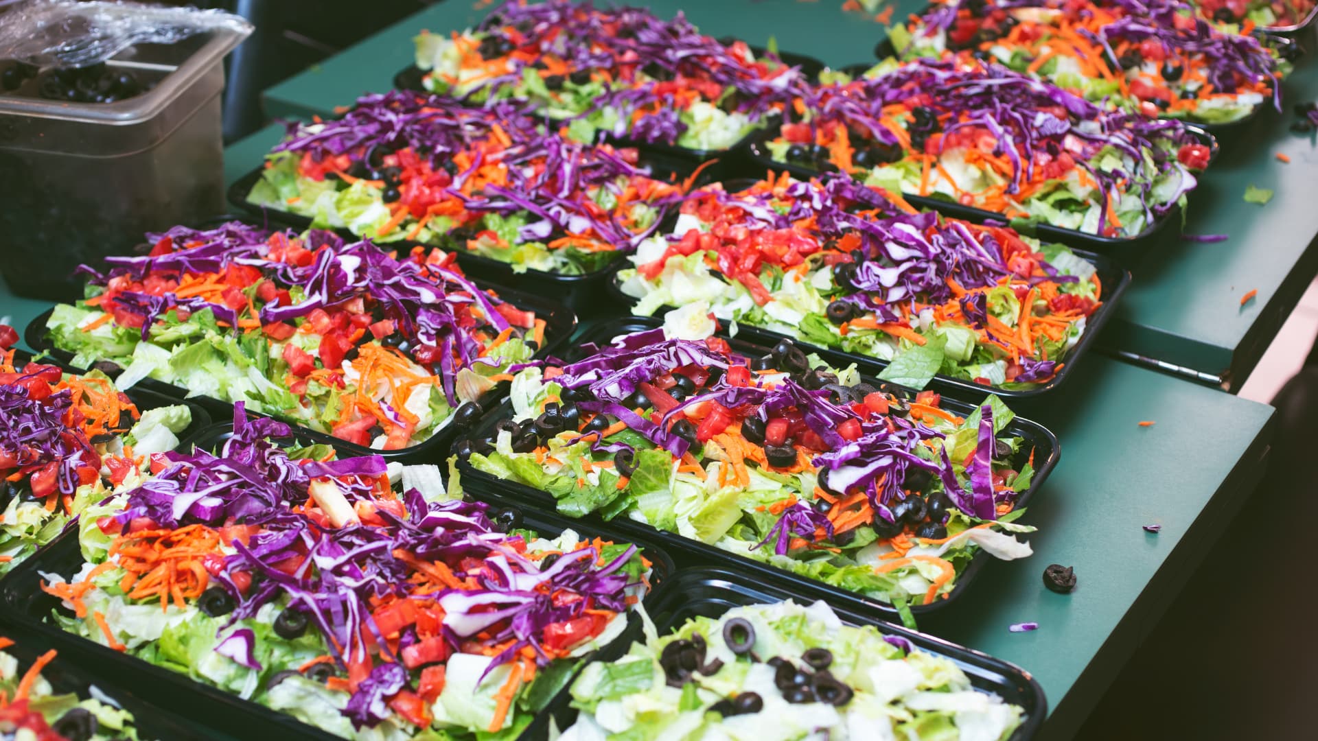 Food Prepped in Commercial Kitchen An image of salad preparation from a stainless steel prep table in a commercial kitchen.